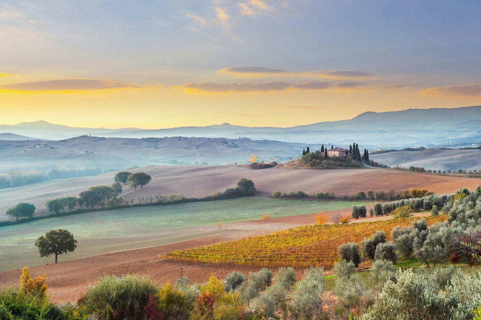 Soft morning light at sunrise over a misty landscape of rolling hills in Tuscany