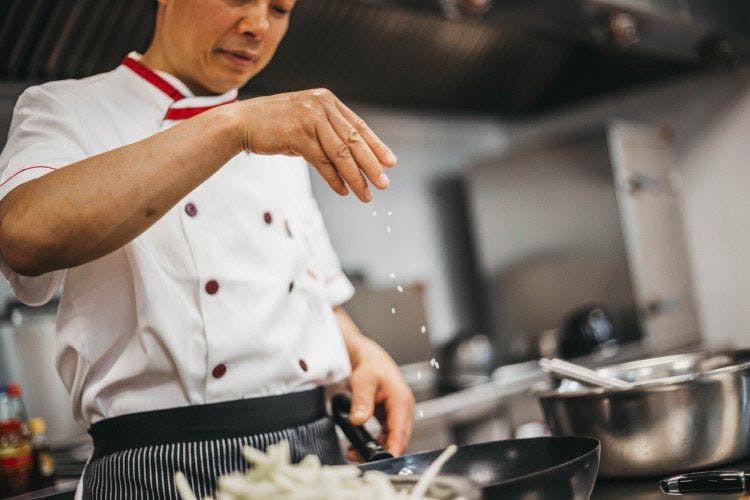 A chef in a white jacket sprinkling salt over a dish