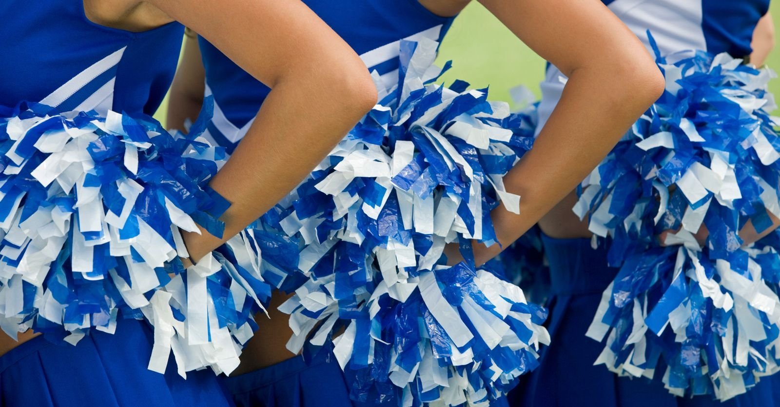 Close up of cheerleaders holding blue and white pom poms by their waists