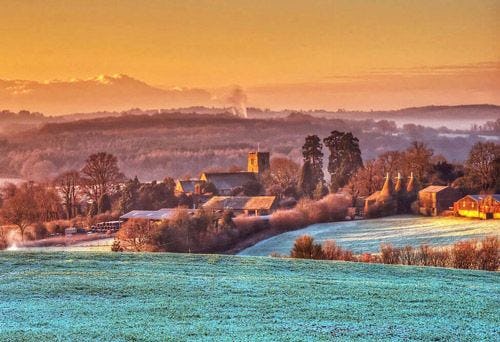 Misty morning in the UK with a traditional stone church and frost-covered fields