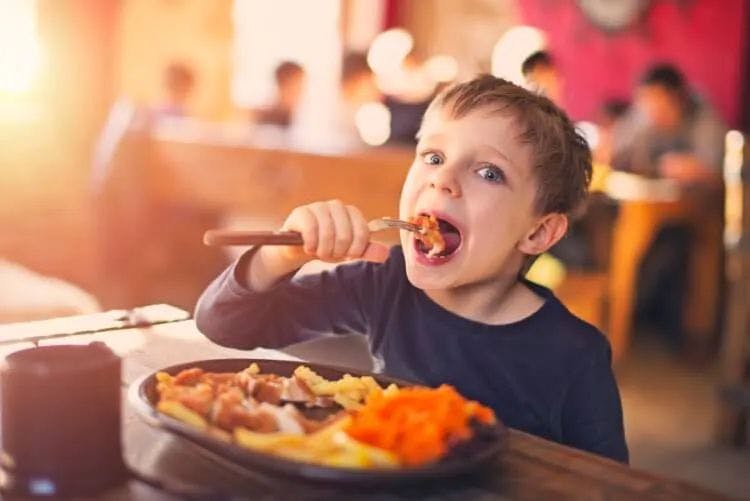 A small boy eating a plate of food in a restaurant