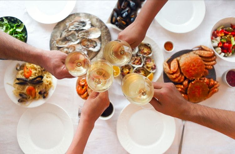 People clinking wine glasses over a table of food