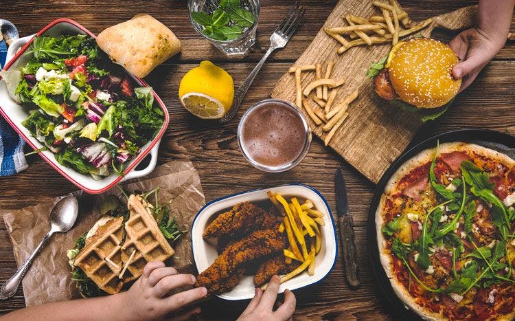 A spread of traditional America food including burgers, fries, chicken, salad, and pizza