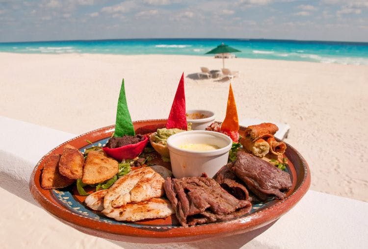A plate of mixed meat and dips on a Cancun beach
