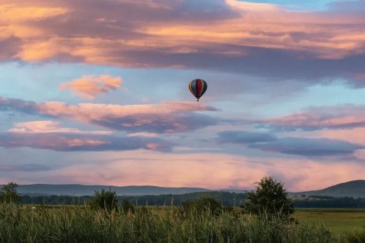 A hot air balloon floats over a field at sunrise