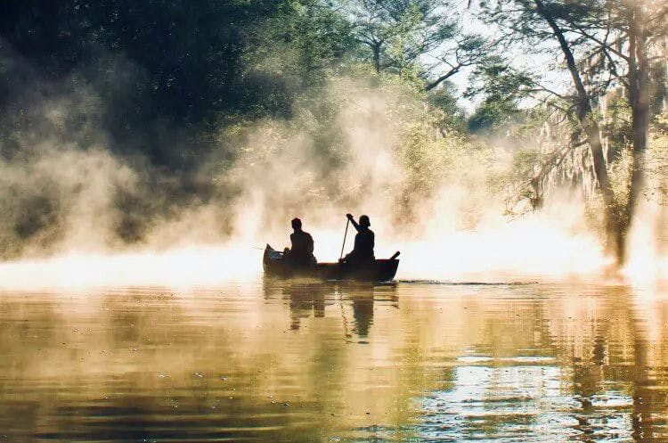 Two people in a kayak drifting through mist in the Florida Everglades