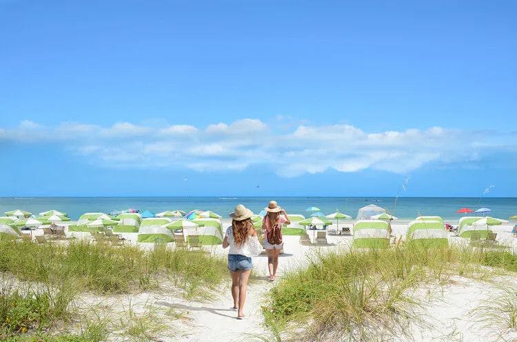 Two women walking along a white sand beach towards sun loungers and parasols by the sea
