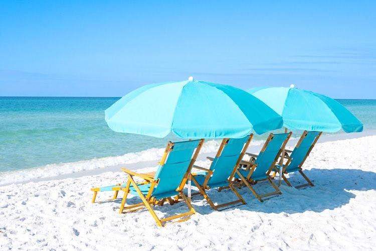 Four blue sun loungers and two parasols on a white sand beach