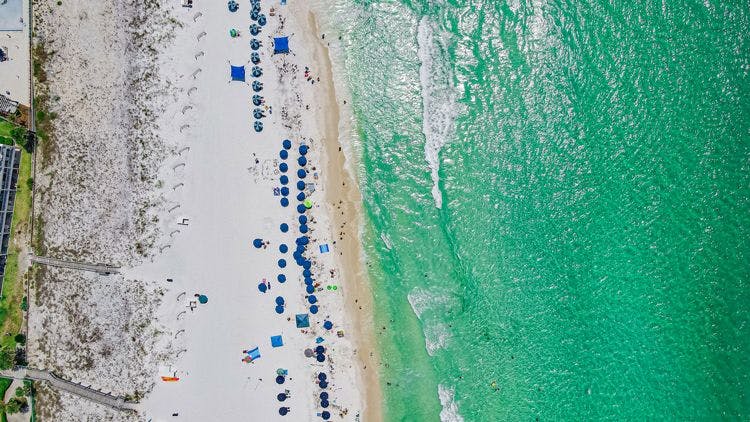 Aerial shot of Destin Beach, with white sand, blue umbrellas and emerald sea