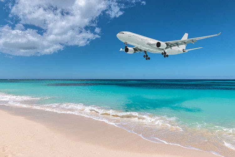 A white passenger plane flying low over a white sand beach