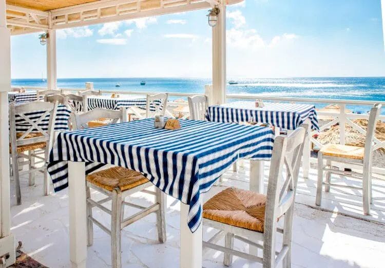 A restaurant by the sea with tables set with navy blue and white striped tablecloths
