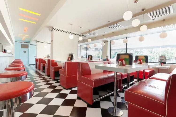 The interior of a traditional American diner with red leather chairs in booths, bar stools, and a black and white checkered floor