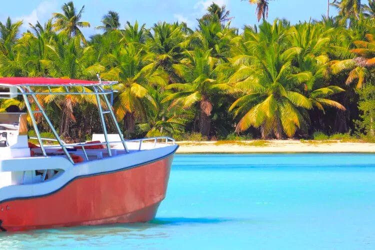 A small red and white boat moored by a white sand beach