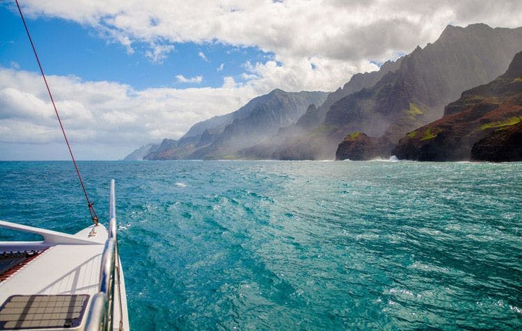 View of the volcanic coast of Hawaii from the front of a catamaran sailing off the coast of Hawaii