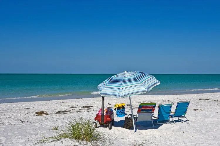 Beach chairs and a parasol on a white sand beach facing calm blue sea