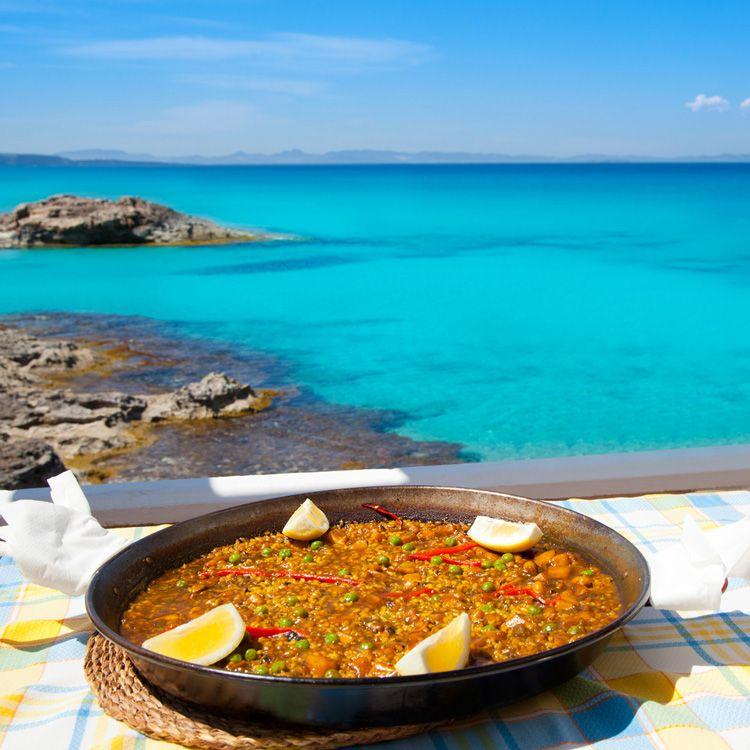 A pan of paella on a table overlooking the sea