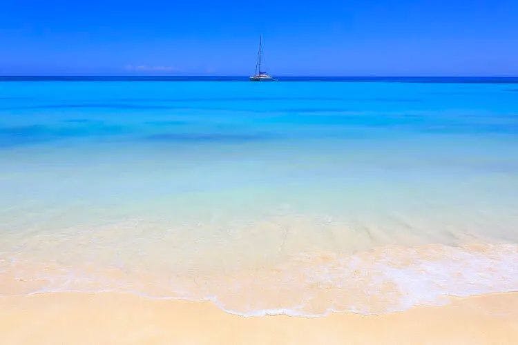 White sand beach and calm, clear sea with a sailboat on the horizon
