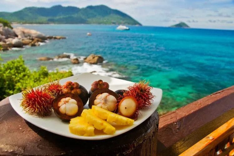 A plate of tropical fruit on a table overlooking the sea