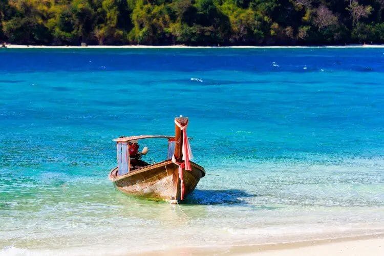 A long tail fishing boat on the shore of a white sand beach
