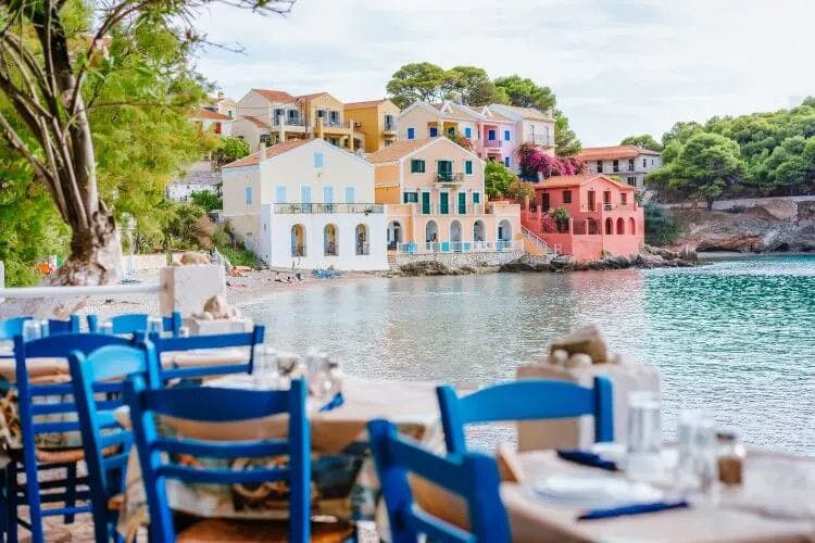 Blue wooden chairs around tables by the water in a colorful Kefalonia town