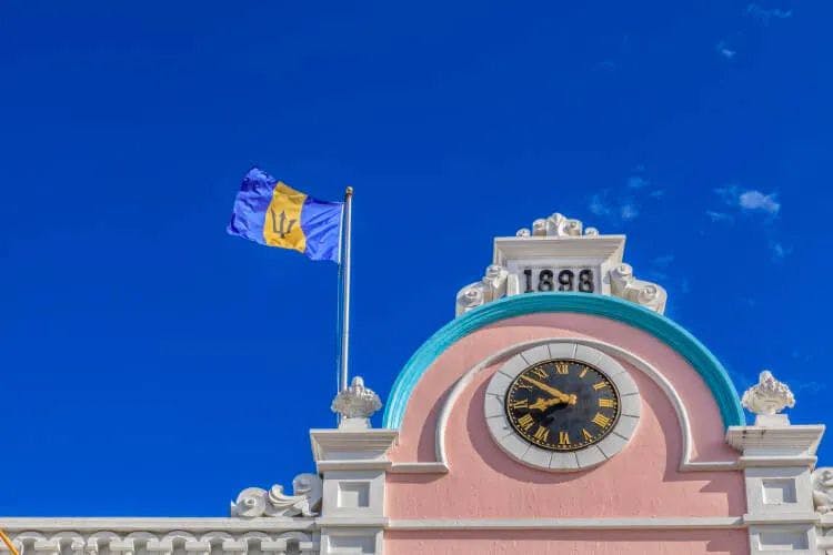 Barbados flag flying over a pink-colored town hall with a clock on it
