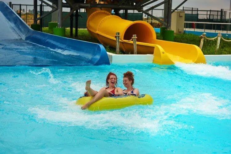 Two women on an inflatable tube in a pool beneath a water slide
