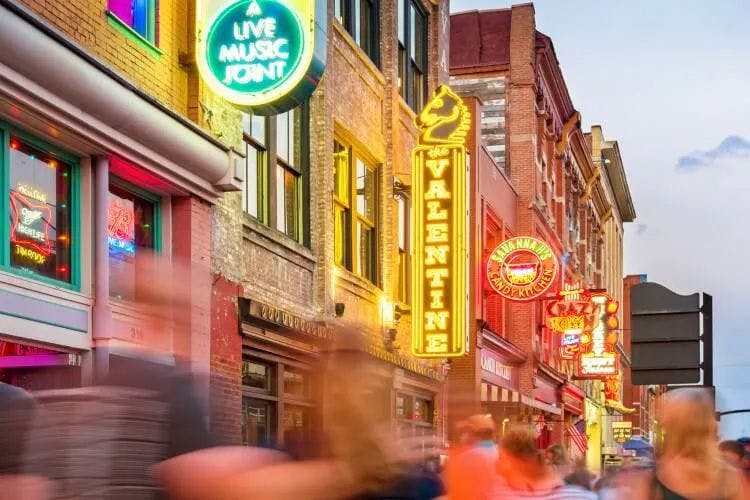 A busy street in Downtown Nashville with neon lights and crowds of people