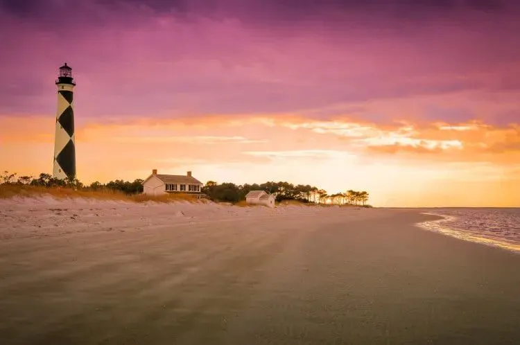 A lighthouse on a beach in North Carolina at sunset