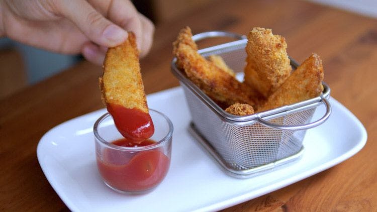 Fried potato wedges being dipped in tomato sauce