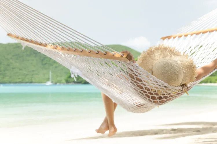 A woman in a large straw hat relaxes in a hammock by the sea