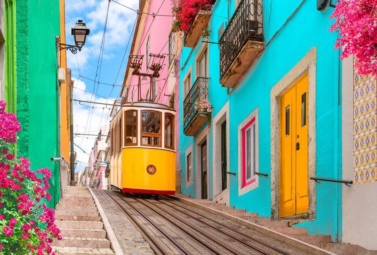 A yellow tram passing brightly colored buildings in Lisbon