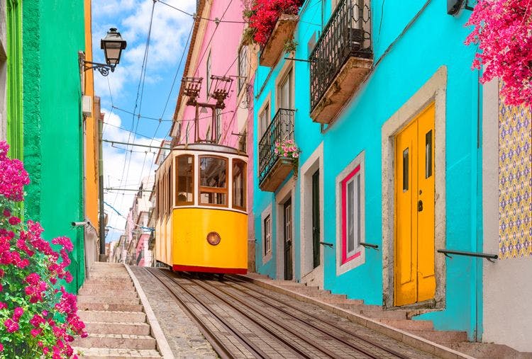 A yellow tram passing brightly colored buildings in Lisbon