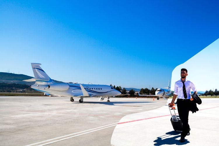 A man in a suit pulls a suitcase across tarmac away from a private jet
