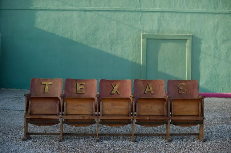 Chairs with letters on them spelling out 'Texas' in front of a green wall