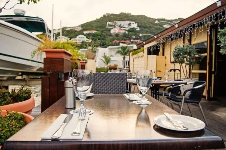 A restaurant table set with cutlery, plates and wine glasses with a view of a tree-covered hillside in Saint Martin