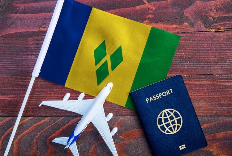 Saint Vincent and the Grenadines flag on a wooden table with model plane and passport