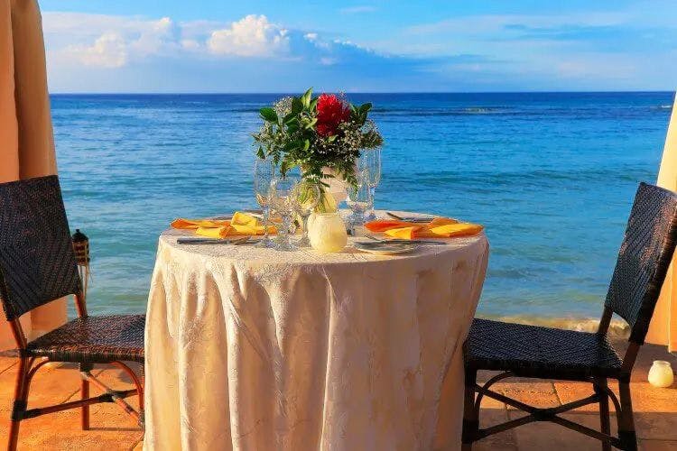 A restaurant table for two with a floral arrangement in the center by the sea