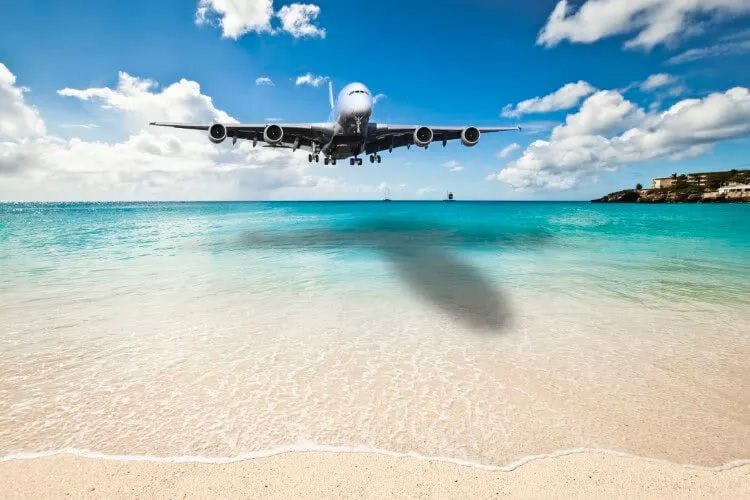 A plane flying low over a beach towards an airport
