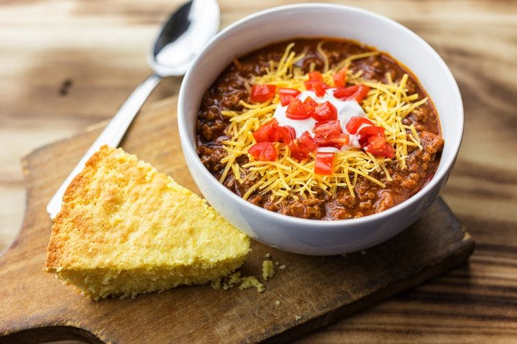 A bowl of cheese-topped- chili and cornbread