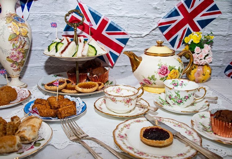 Afternoon tea spread with traditional English food including jam tarts, sausage rolls, and finger sandwiches