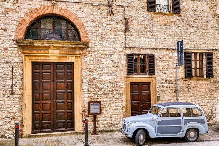 A vintage car parked outside a large town hall building with wooden doors in Umbria