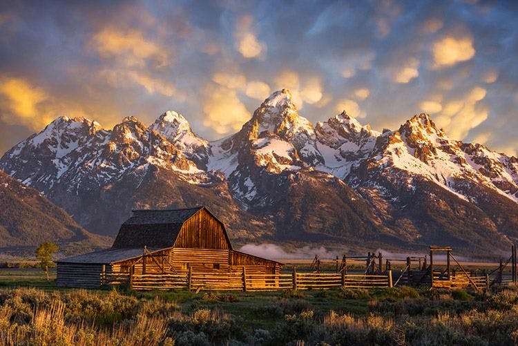 Snow-capped mountains behind a wooden barn in Wyoming