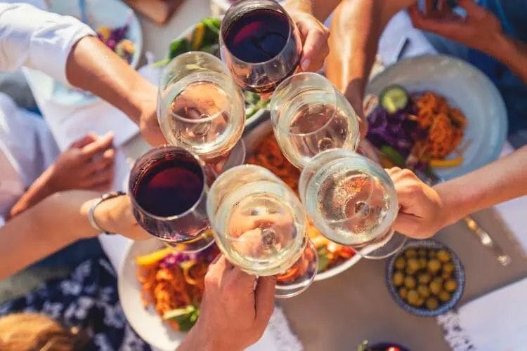 People cheersing wine glasses over a table of food