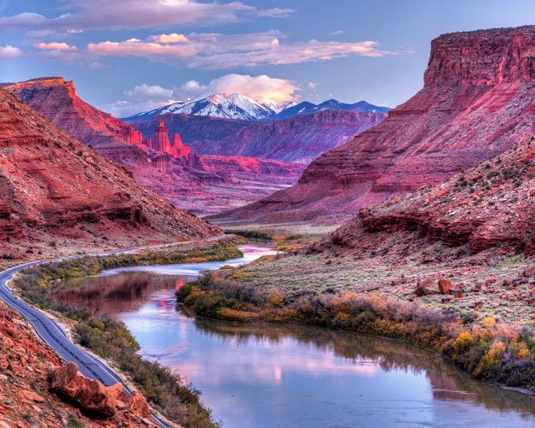 View of Utah landscaoe with still river running through a canyon and snow capped mountain in the background