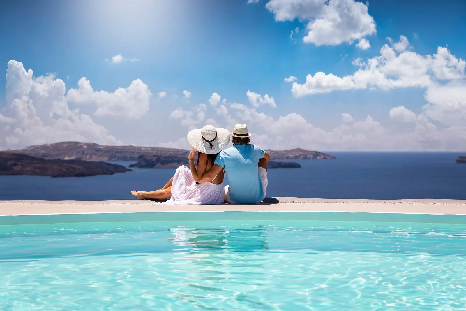 A couple sitting by a pool looking over the Aegean Sea in Greece
