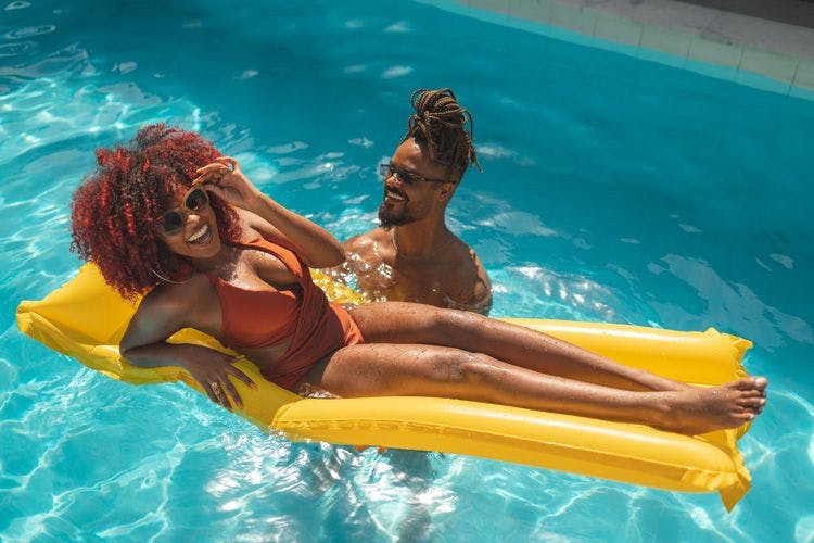 A young couple in a private pool - the lady wears a bronze swimsuit and floats of a yellow inflatable