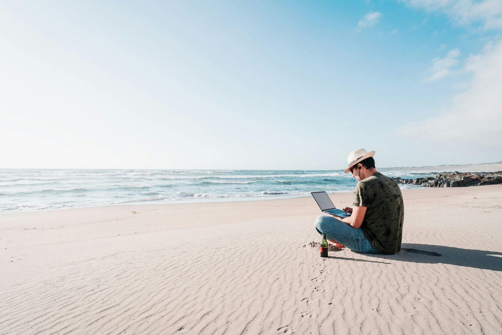 A man sitting on a beach working on a laptop