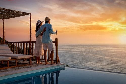 A couple standing on a wooden balcony watching a sunset over the sea
