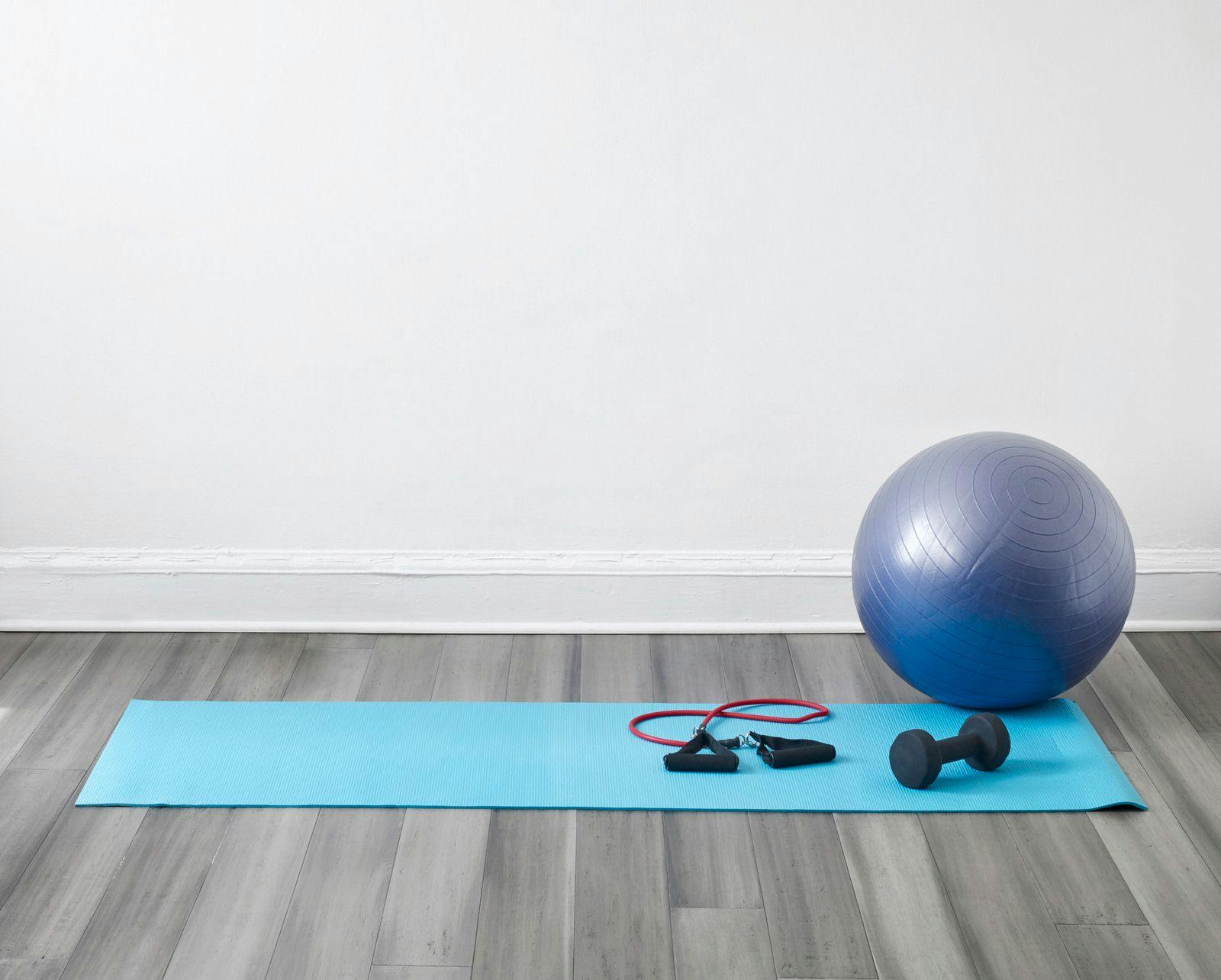 Gym equipment including a blue yoga mat, inflatable balance ball and dumbbells 