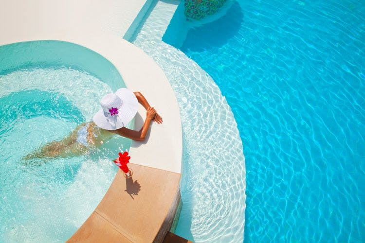 A lady in a large hat lies in a hot tub by a pool